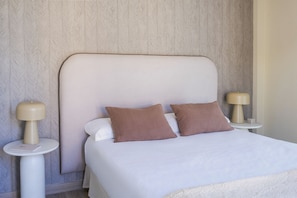 A neatly made bed with two pillows, a bedside table with a lamp, and a patterned wall. - Housing Atarazanas by Sharingco (Málaga)
