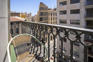 A balcony with a wicker chair, overlooking a cityscape with various buildings and a clear sky. - Housing Atarazanas by Sharingco (Málaga)