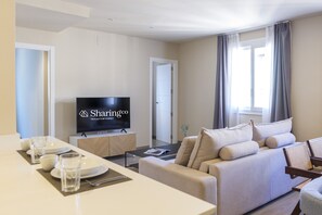 A modern living room with a sofa, a flat-screen TV, and a dining area with a table set for two. - Housing Atarazanas by Sharingco (Málaga)