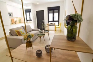 A modern living room with a sofa, coffee table, and decorative items. There is a kitchen area in the background with cabinets and a microwave. - Housing Ollerias by Sharingco (Málaga)