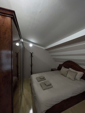 Une chambre avec un plafond en pente, une armoire en bois, un lit avec des oreillers et des serviettes pliées, et un porte-manteau.