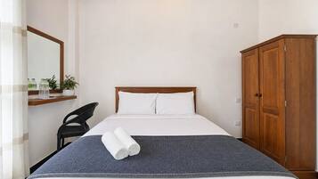 Una habitación de hotel con cama, armario, silla, espejo y estante con artículos de aseo.