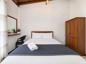 A hotel room with a bed, a wardrobe, a chair, a mirror, and a shelf with toiletries. - Villa Nira (Galle)