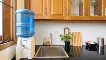 A kitchen with wooden cabinets, a water dispenser, a sink, a potted plant, a cutting board, and a coffee maker.
