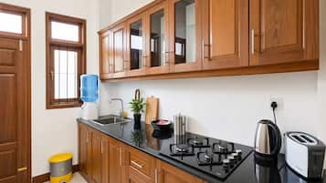 Una cocina con armarios de madera, encimera negra, dispensador de agua, fregadero, estufa, hervidor y tostadora.