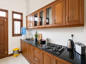 A kitchen with wooden cabinets, a black countertop, a water dispenser, a sink, a stove, a kettle, and a toaster.