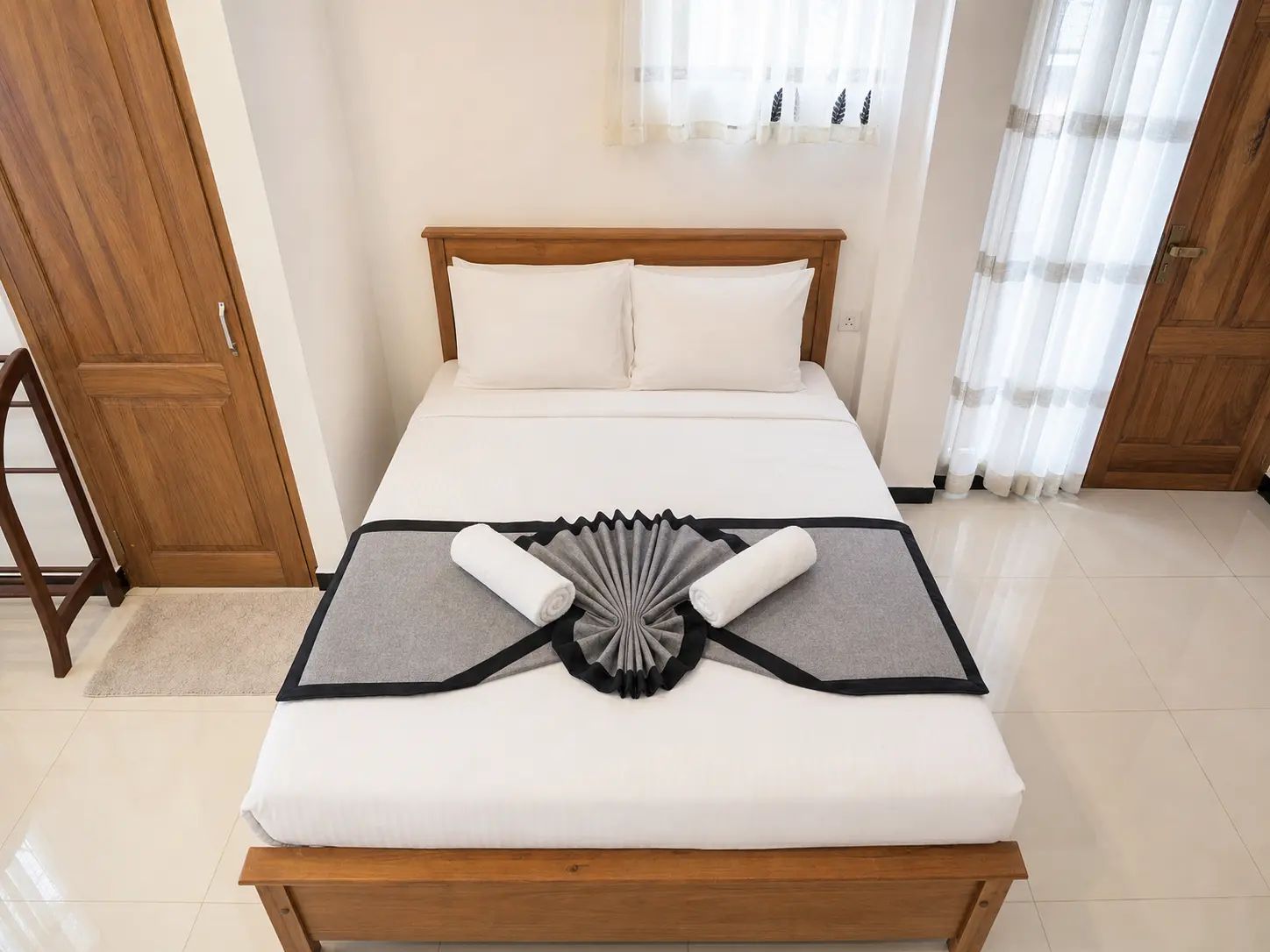 Una cama bien hecha con un adorno gris y negro sobre el edredón, un cabecero de madera y almohadas blancas.