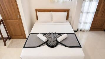 Una cama bien hecha con un adorno gris y negro sobre el edredón, un cabecero de madera y almohadas blancas.