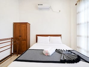 A hotel room with a bed, a wooden wardrobe, a wall-mounted air conditioner, and a window with sheer curtains.
