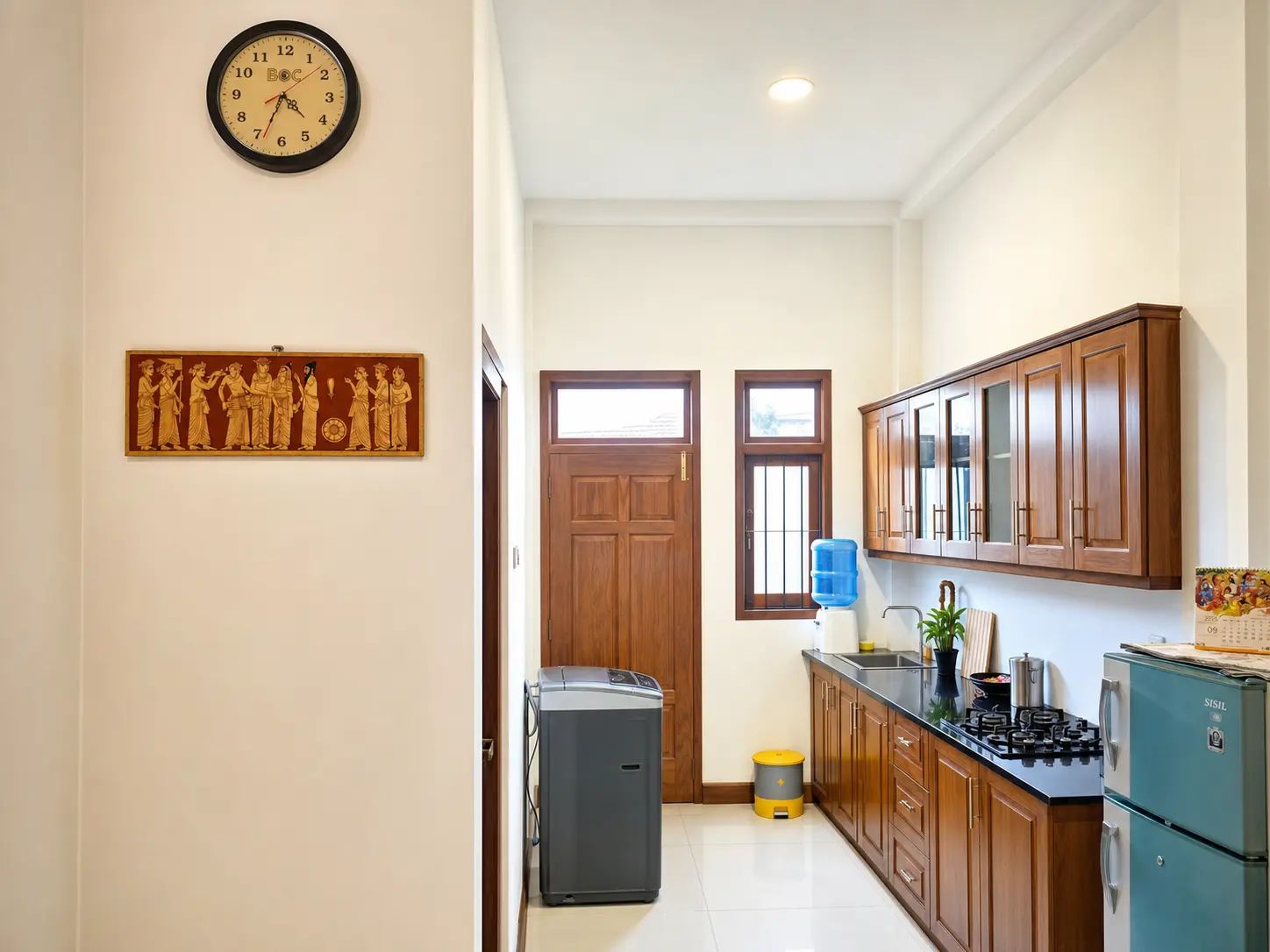 Una cocina con armarios de madera, dispensador de agua, refrigerador y un reloj en la pared.