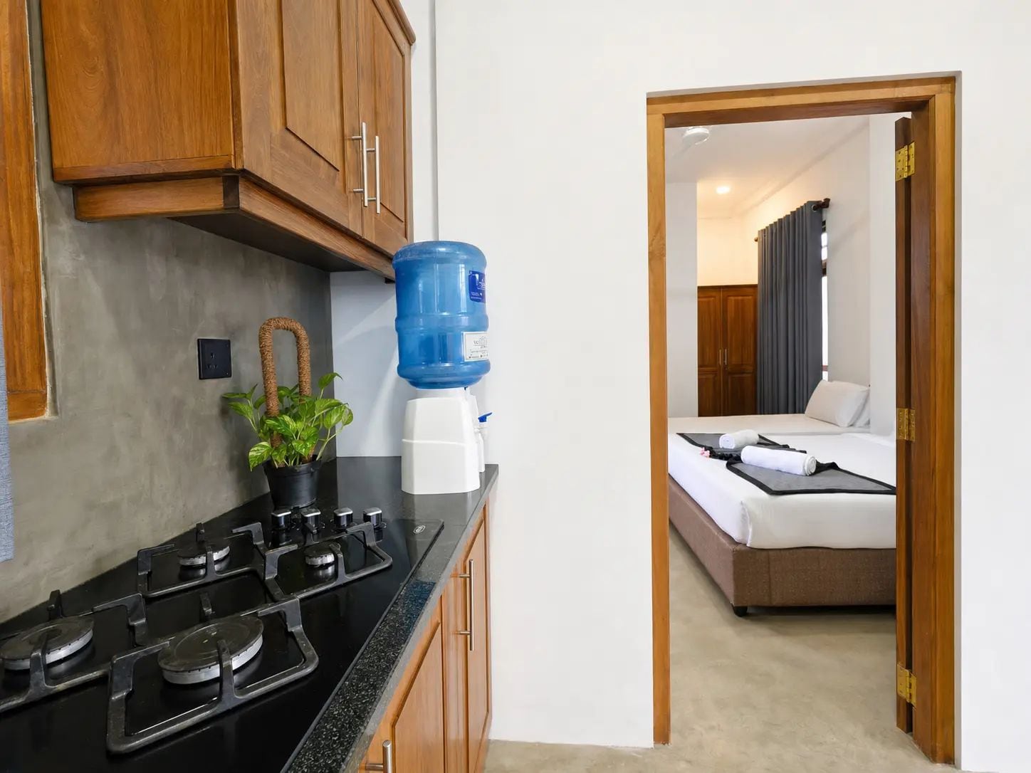 Cocina compacta con estufa a gas, dispensador de agua y una planta en maceta.