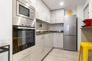 A modern kitchen with stainless steel appliances, white cabinetry, and a yellow stool. - El Limonar by Sharingco (Málaga)
