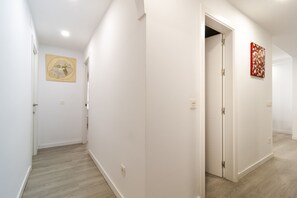 A hallway with white walls, a wooden floor, and two doors. One door is open, revealing a room with a red and white abstract painting. - El Limonar by Sharingco (Málaga)