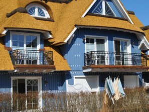 A two-story house with a thatched roof, white-framed windows, and a balcony with a metal railing. - Evening - Apartment 4 (Zingst)
