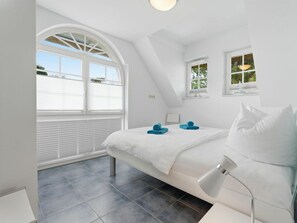 A bedroom with a bed, two windows, a ceiling light, and a bedside table. - Evening - Apartment 4 (Zingst)