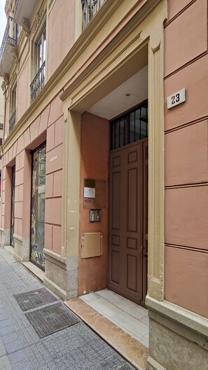 A building with a large brown door, a number '23' sign, and a small window with a sign above it. - Mlgsa023san4a - San Lorenzo (Málaga)