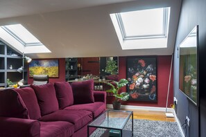 Un salon moderne avec un canapé rouge, des fenêtres de toit, un grand tableau et une plante en pot.