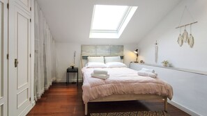 A bedroom with a skylight, a bed with pillows and towels, a bedside table with a lamp, and a wall-mounted cross. - Mlgsa023san4a - San Lorenzo (Málaga)
