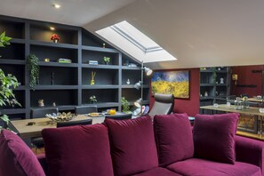 A modern living room with a dark wood table, a purple sofa, and a skylight above a shelving unit with plants and books. - Mlgsa023san4a - San Lorenzo (Málaga)