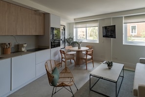 Eine moderne Küche mit weißen Schränken, einem Essbereich mit rundem Tisch und Stühlen sowie einem an der Wand montierten Fernseher.