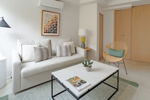 Ein modernes Wohnzimmer mit einer Couch, einem Couchtisch, einem Sessel, einer Lampe und einem gerahmten Bild an der Wand.
