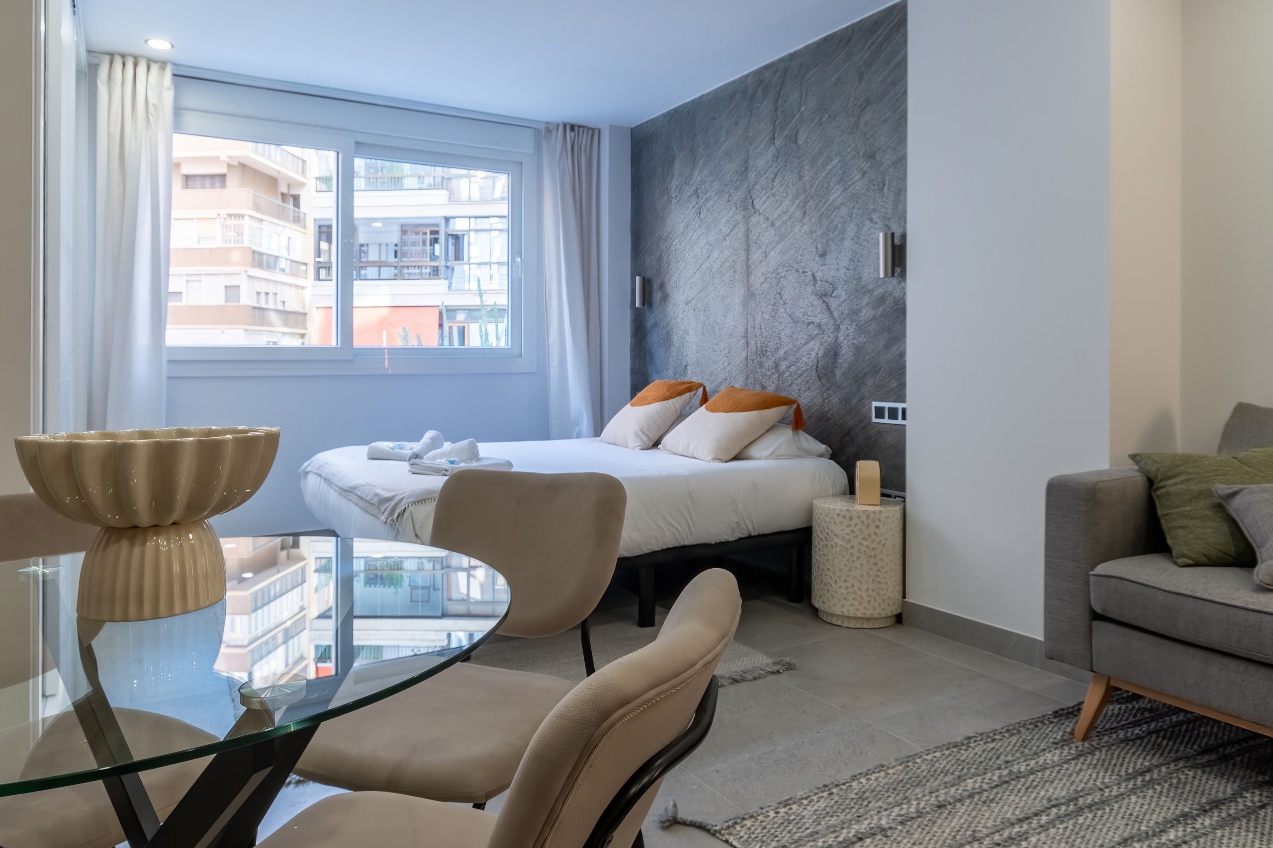 A modern hotel room with a large bed, a glass table, and a sofa.
