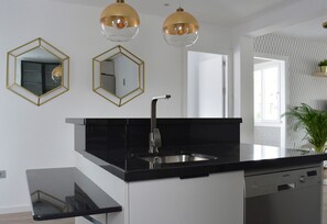 A modern kitchen with a black countertop, gold-framed mirrors, and pendant lights. - Mlgsa032gra7izq - Calle Granada (Málaga)