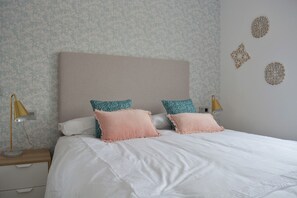 A neatly made bed with two pillows, a bedside lamp, and a wall with decorative elements. - Mlgsa032gra7izq - Calle Granada (Málaga)