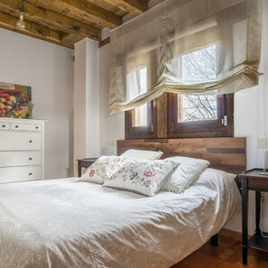 A bedroom with a wooden headboard, a bed with floral bedding, a white dresser, and a window with curtains. - Segsa000ntimtt - Segovia (Turegano)