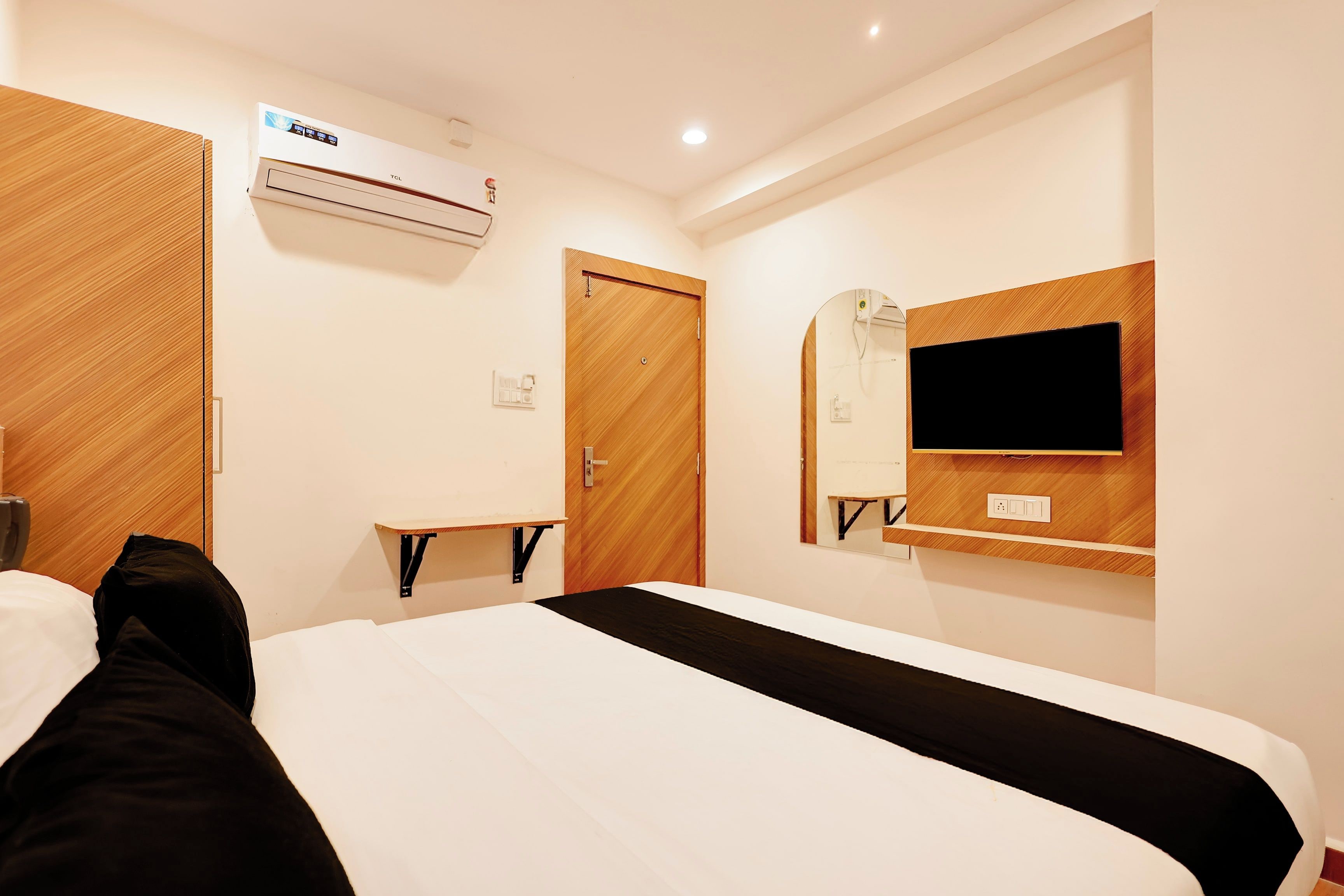 A hotel room with a bed, a TV mounted on the wall, an air conditioning unit, and a wooden door.
