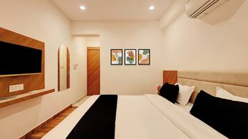 A hotel room with a bed, a flat-screen TV, a mirror, and two framed artworks on the wall.