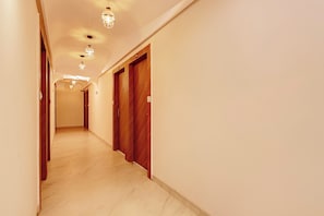 A hotel hallway with wooden doors, a light-colored floor, and ceiling lights. - Super Townhouse Dewas Bus Terminal (Ujjain)
