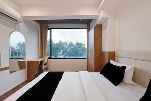 A hotel room with a large bed, a desk, a chair, a window with a view of trees, and a mirror. - Super Townhouse Dewas Bus Terminal (Ujjain)