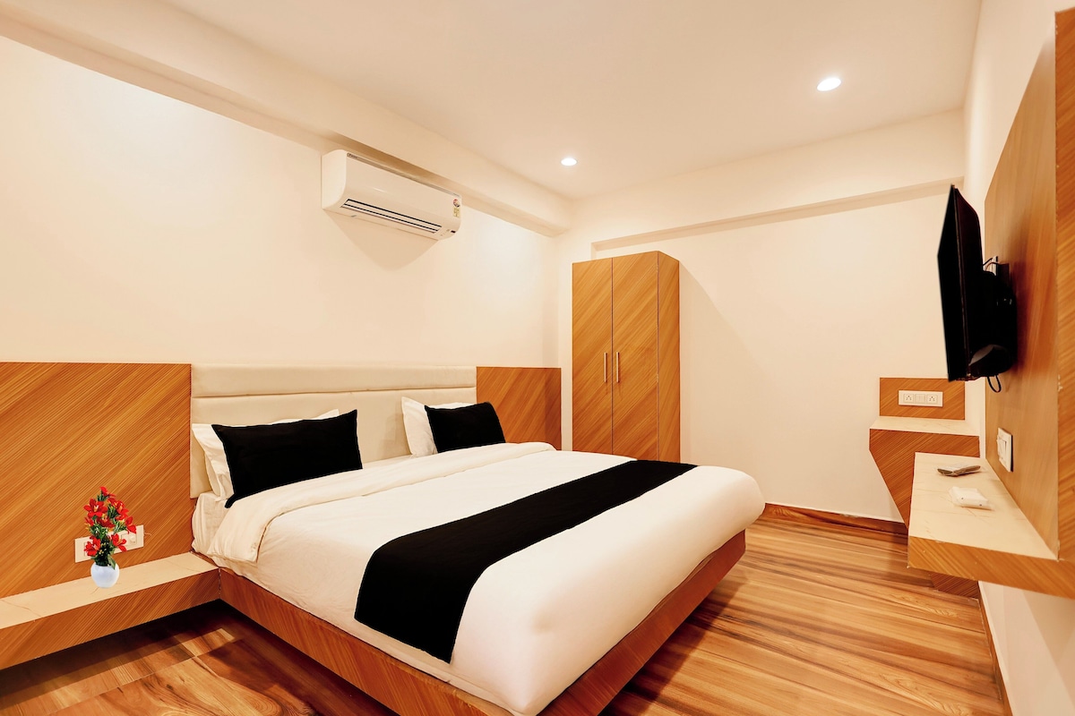 A hotel room with a bed, bedside table, TV, wardrobe, and an air conditioning unit.