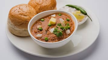 A bowl of curry with bread and a lemon wedge on a plate.