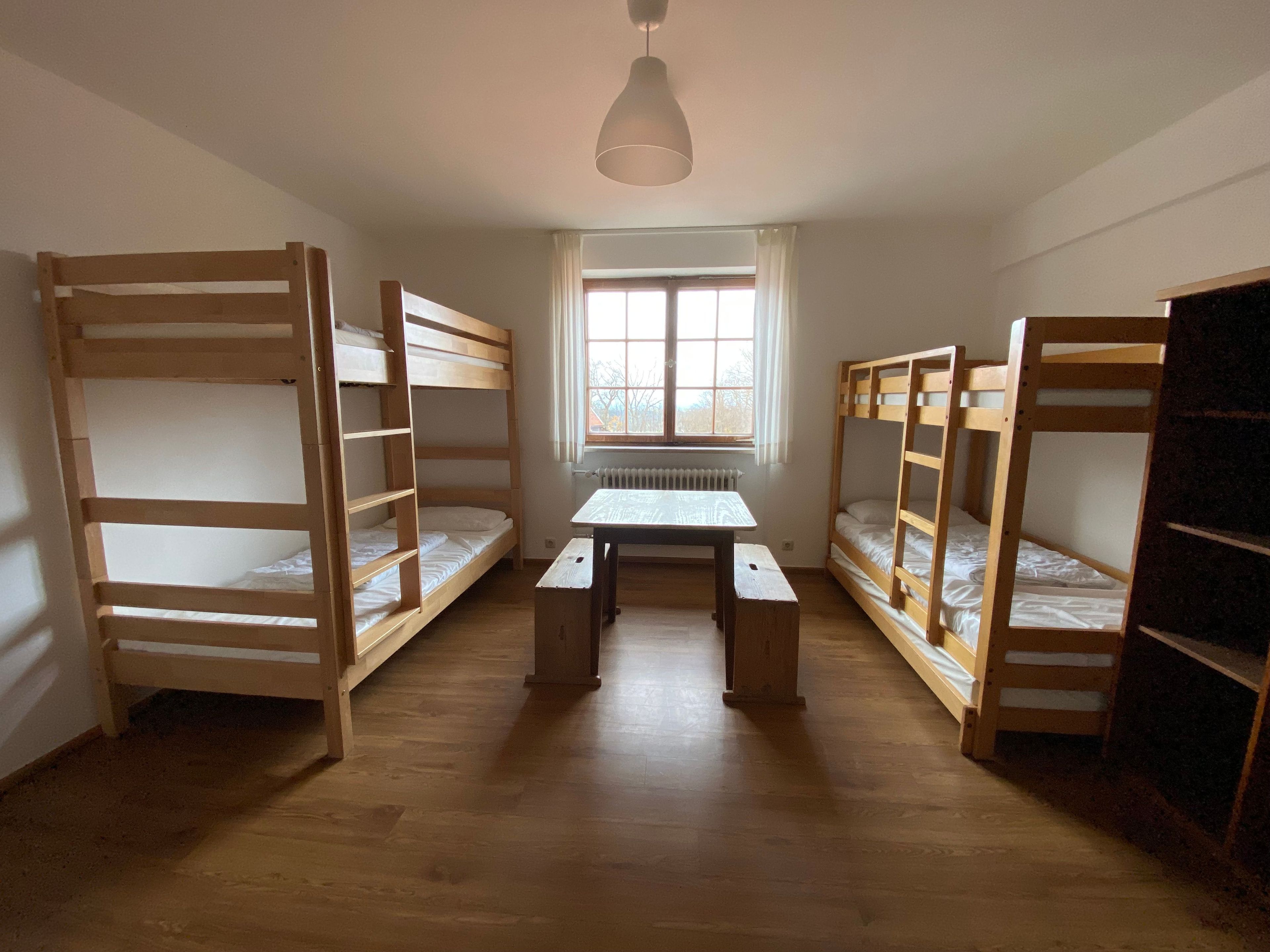 Ein Zimmer mit Etagenbetten, einem Tisch und einem Fenster.