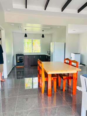 Une cuisine moderne avec un coin repas, comprenant une grande table et des chaises en bois, un four encastré et un réfrigérateur.