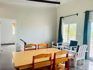 Une pièce moderne avec une table et des chaises de salle à manger en bois, un ensemble de canapés blancs et une grande fenêtre avec des rideaux.
