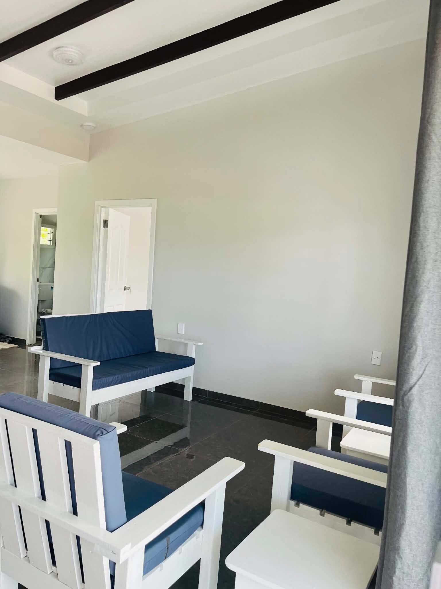 Una habitación con muebles blancos, incluyendo un sofá y sillas, y una puerta que da a otra zona.