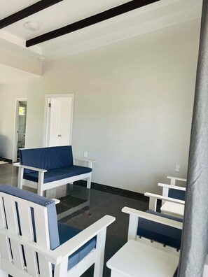 Une pièce meublée de blanc, avec notamment un canapé et des fauteuils, et une porte donnant sur un autre espace.