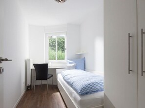 Ein Schlafzimmer mit einem Einzelbett, einem Sessel, einem Fenster und einer Heizung.
