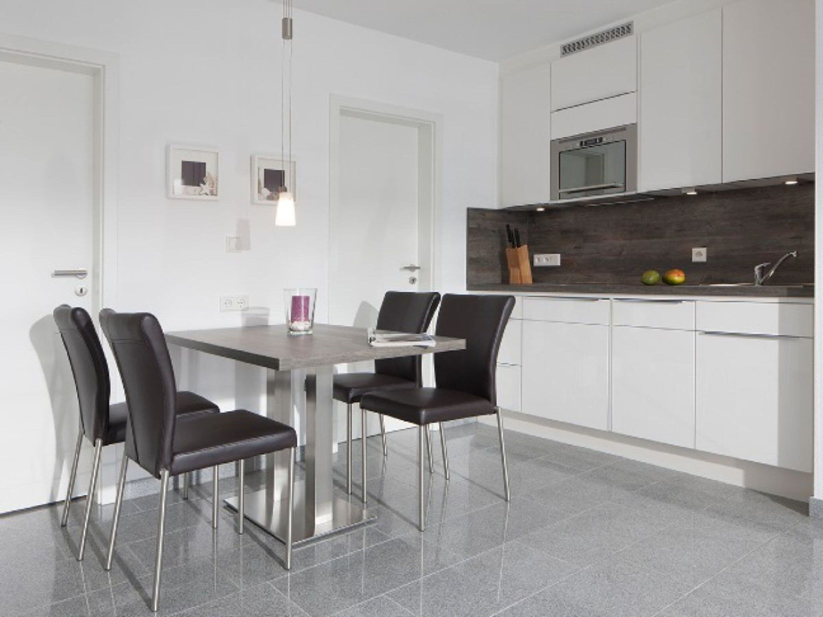 Une cuisine moderne avec une table à manger, des chaises, un luminaire suspendu et un four encastré.