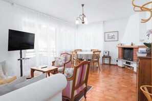 A living room with a TV, a fireplace, and a dining area with chairs and a table. - 2BR with Balcony and Mountain Views near Lugano (Magliaso)
