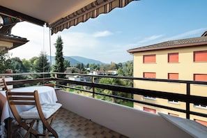 A balcony with a table and chairs, overlooking a residential area with buildings and mountains. - 2BR with Balcony and Mountain Views near Lugano (Magliaso)