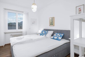 Quarto com cama, mesa de cabeceira, janela e radiador.