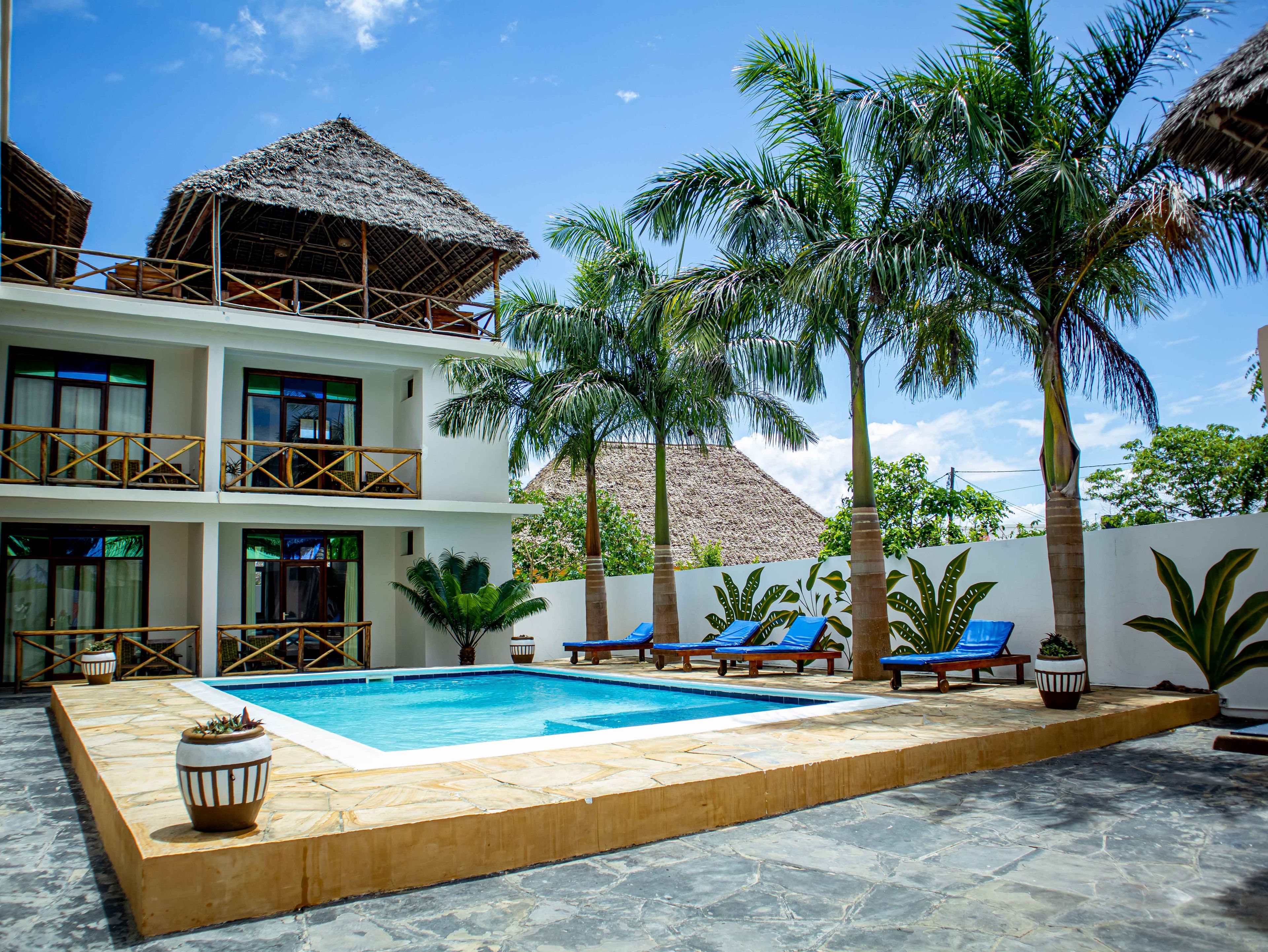 A two-story building with a swimming pool, lounge chairs, and palm trees.