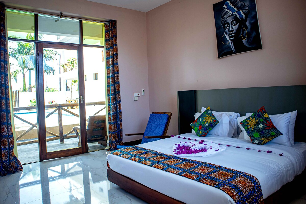 A hotel room with a bed, a painting, and a view of a pool area.