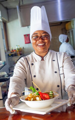 A chef in a white uniform with a tall hat, holding a bowl of food. - Double A Nungwi Seaview Hotel (Nungwi)
