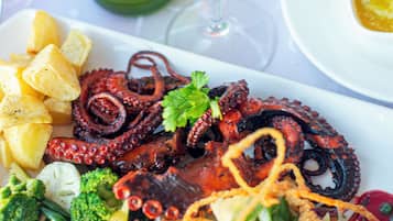 Un plato de pulpo a la parrilla con verduras y patatas, una copa de vino blanco y una botella de vino con un diseño de jirafa.