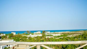 A coastal view with buildings and greenery, a clear sky, and a wooden railing in the foreground.